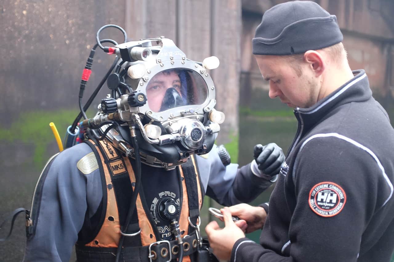 diver wearing a diver's helmet assisted by a diving staff